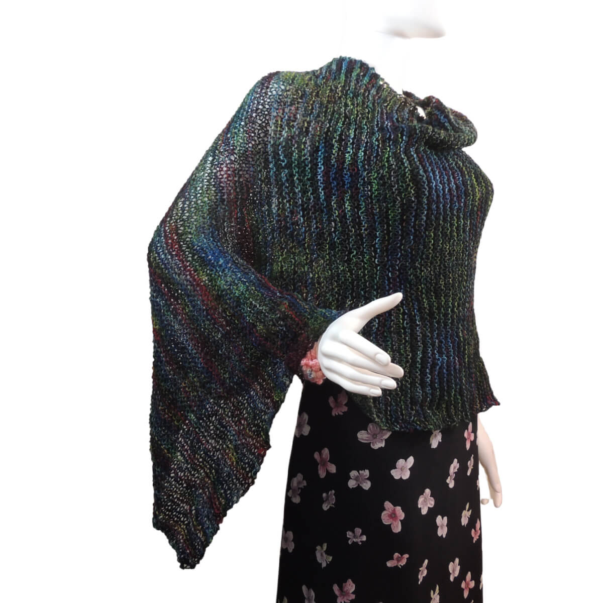 White mannequin wearing a black tank and skirt and a knit poncho in black with bits of dark red, blue, and green. The poncho is waist length and straight across the front with a point hanging off one arm.