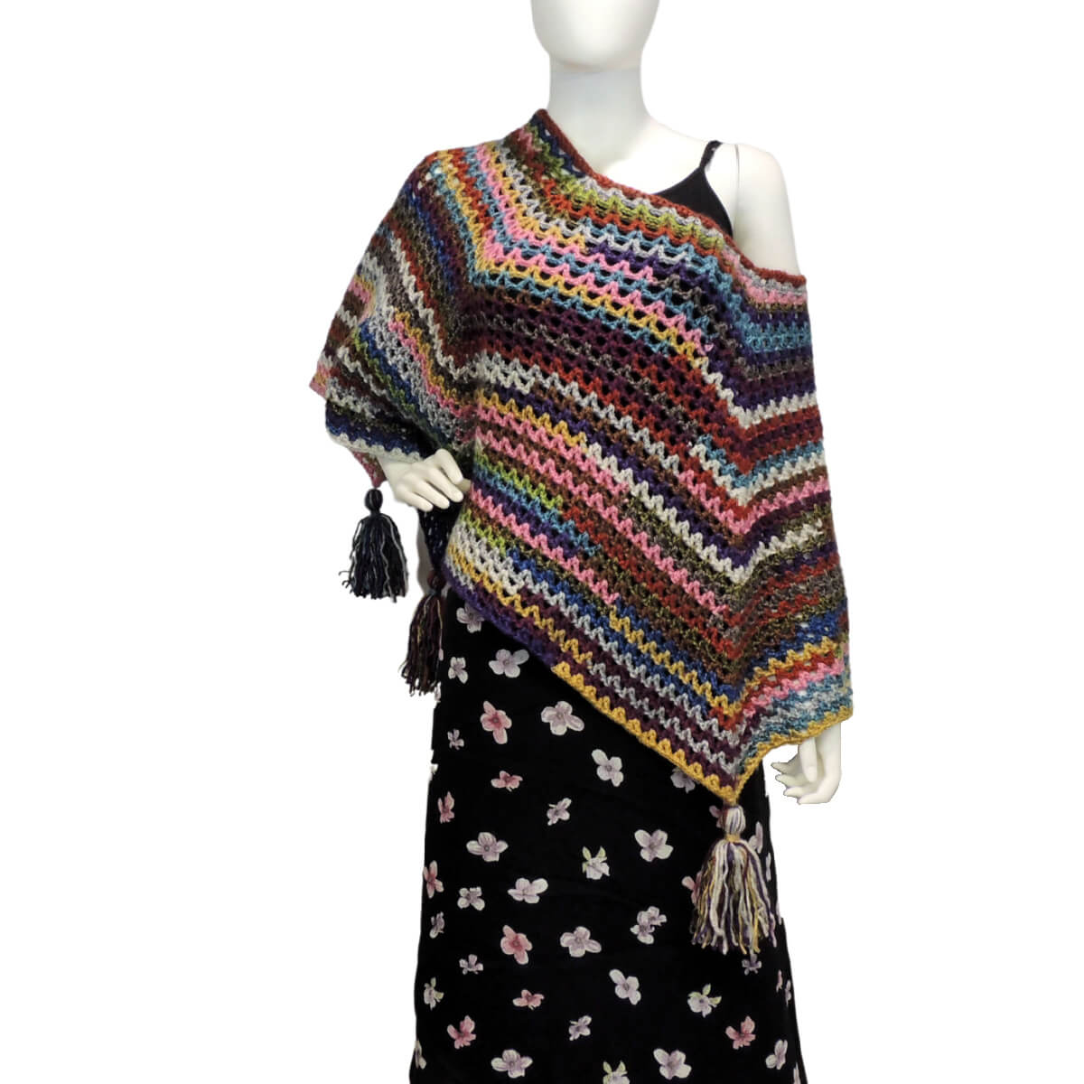 Front of a mannequin wearing a black skirt and a multicolor V-stitch crochet square poncho with large tassels hanging from each of the 4 points. The points all hang at the sides and the poncho neck is pulled to one side so it hangs over the shoulder of the mannequin.