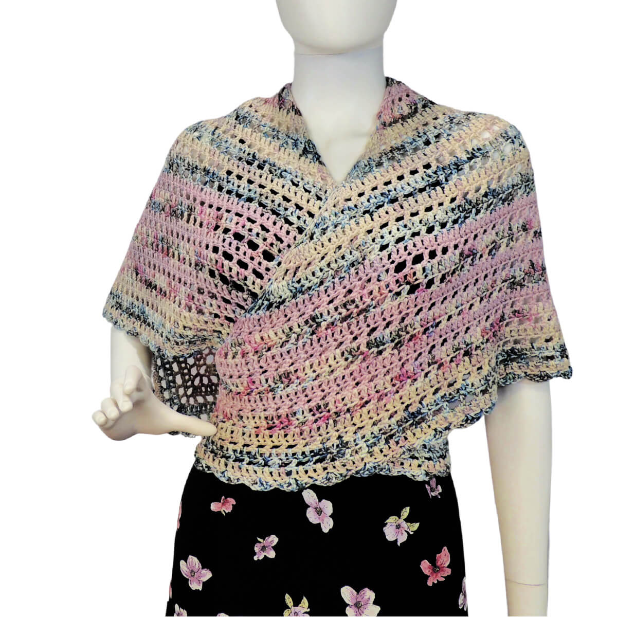 Front view of a white mannequin in a black skirt, black tank top, and a triangular shawl that's almost a 45/45/90 triangle, but is slightly off so all 3 sides and angles are different. The shawl is crocheted in alternating rows of solid stitches and mesh stitches in yarn lightly colored in shades of pale pink, pale blue and pale yellow. The 2 shorter of the 3 sides have a scalloped border. The center of the long side of the shawl is behind the neck and the two sides wrap one at a time around the front then around to the back so they overlap in front.